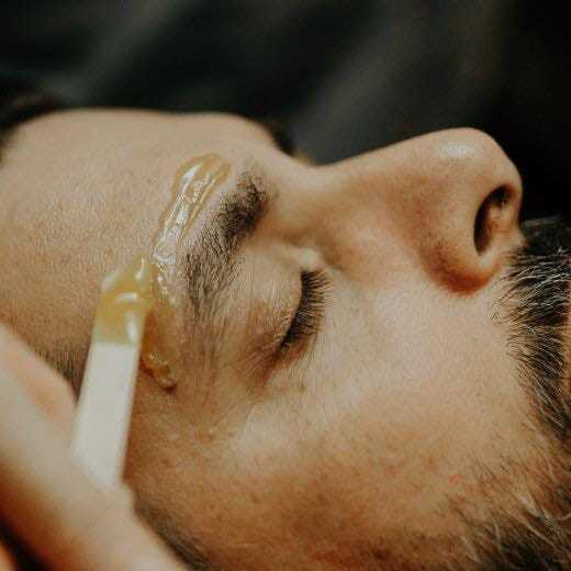 Man receiving eyebrow grooming treatment with wax applied on the brow.