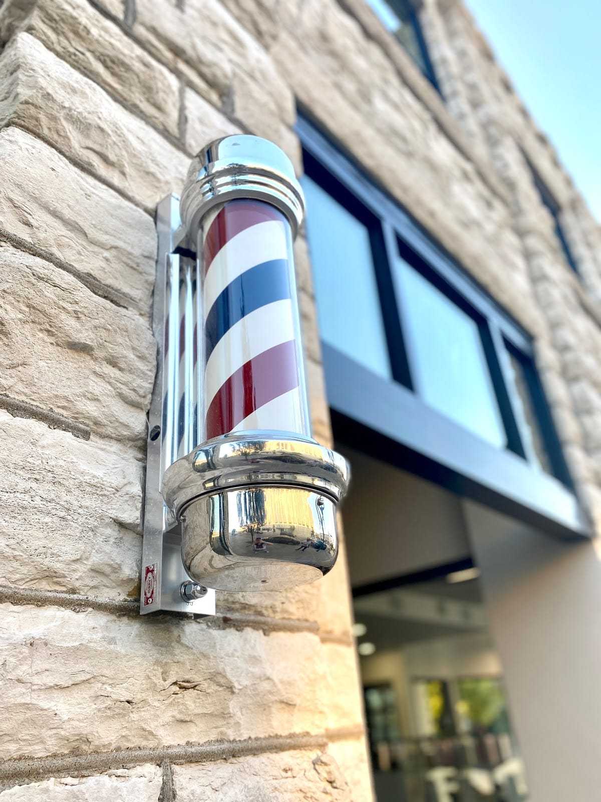 Barber pole attached to stone wall, with window and doorway visible.