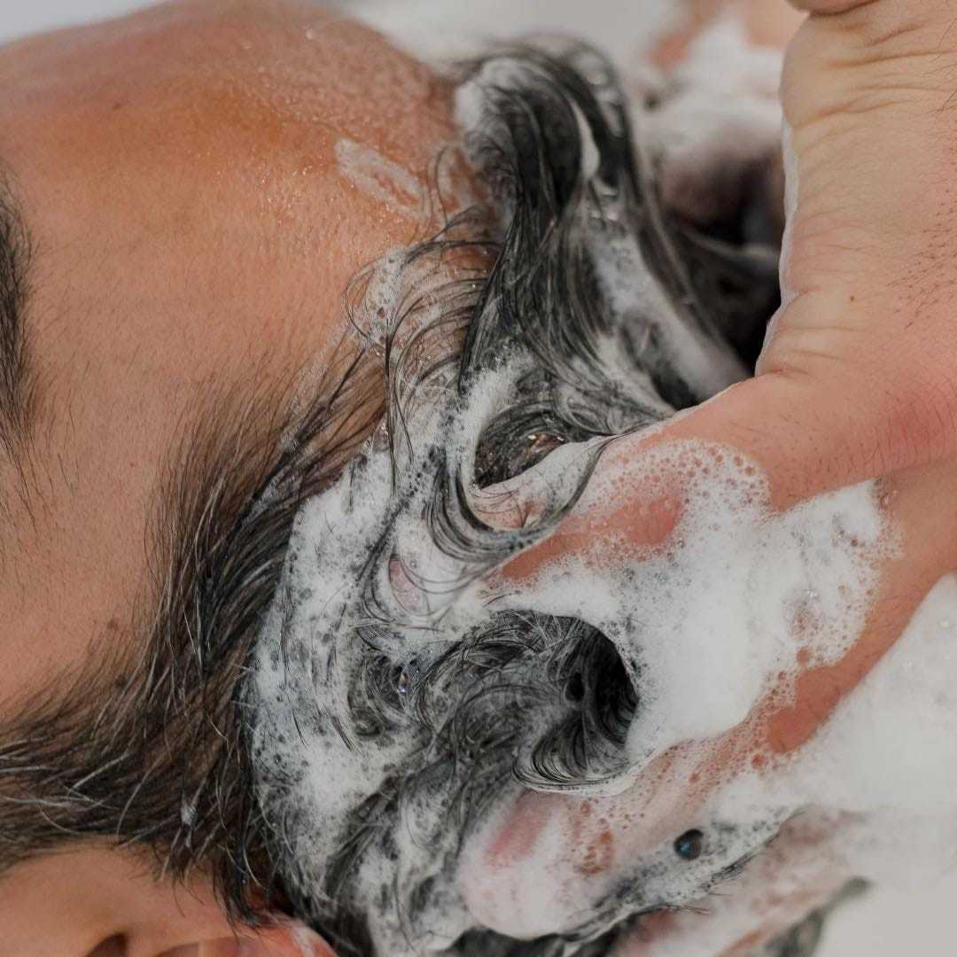 Person's head receiving a shampoo massage, with lathered soap.
