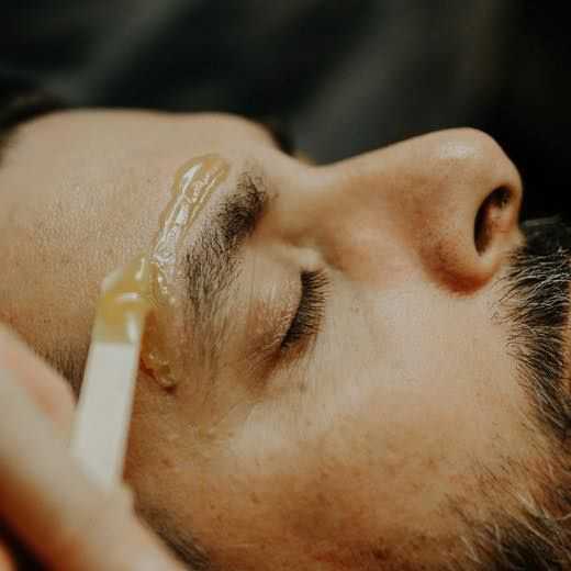 Man receiving eyebrow grooming treatment with wax applied on the brow.